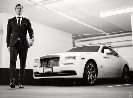 brooks in a black suit beside a white rolls royce